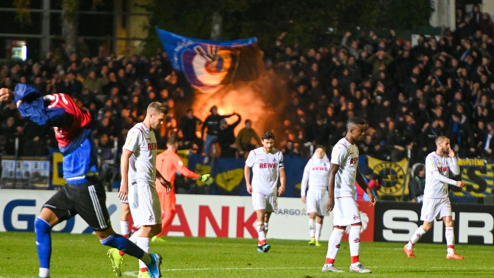 Die Spieler des 1. FC Köln lassen die Köpfe hängen, die Saarbrücken-Fans zünden Pyrotechnik.