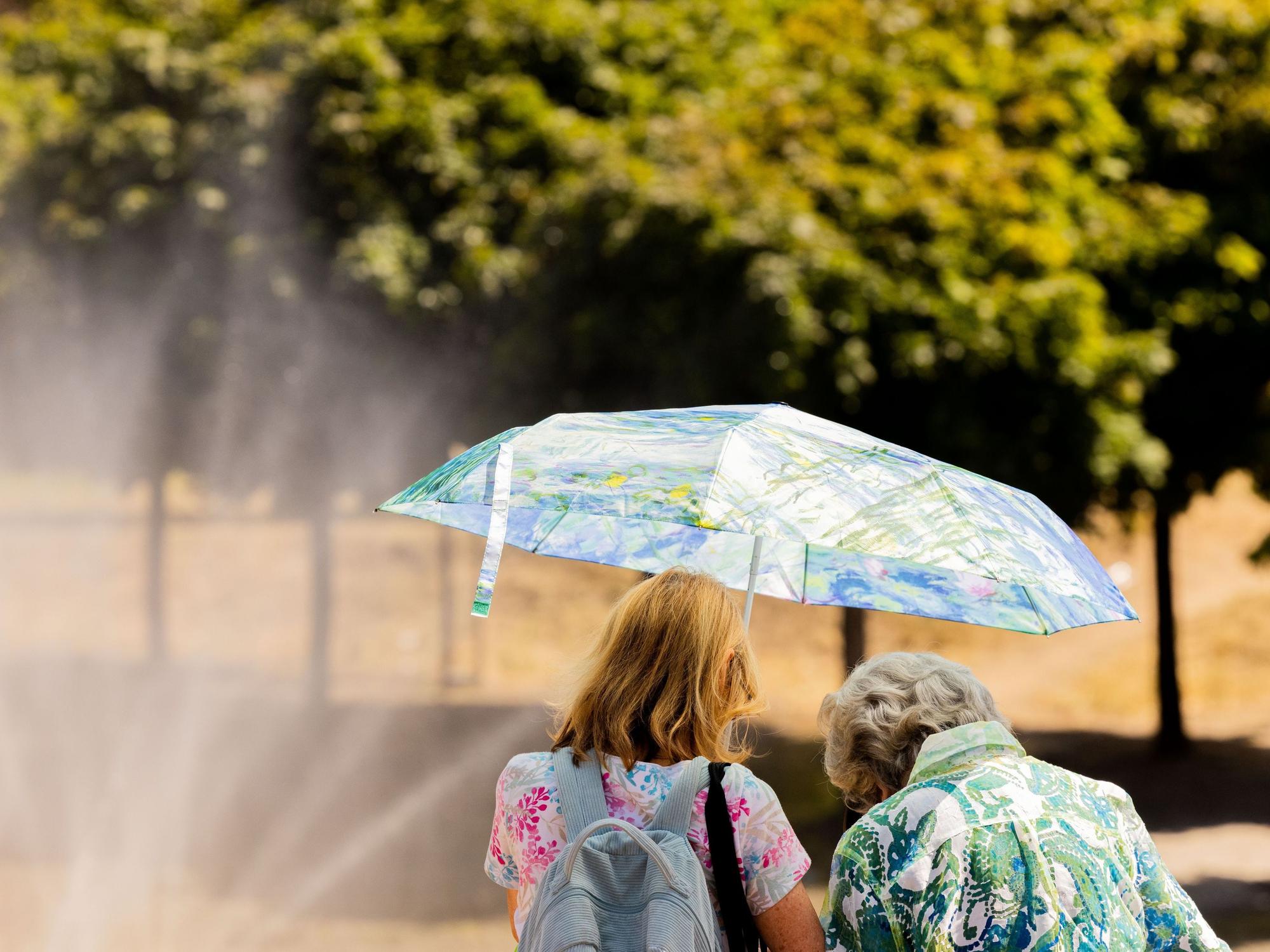 Zwei Frauen schützen am Rheinufer in der Altstadt mit einem Regenschirm vor der Sonne.