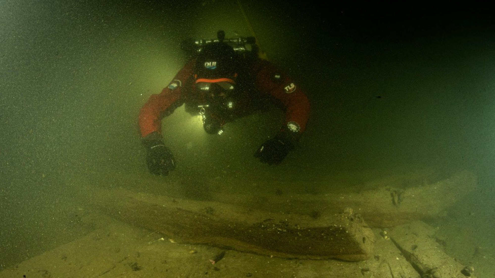 Ein Taucher benutzt in der Trave bei der Begutachtung von Planken eines Schiffswracks eine Unterwasserlampe. Auf dem Grund wurde ein rund 400 Jahre altes Wrack eines Hanseschiffs gefunden.