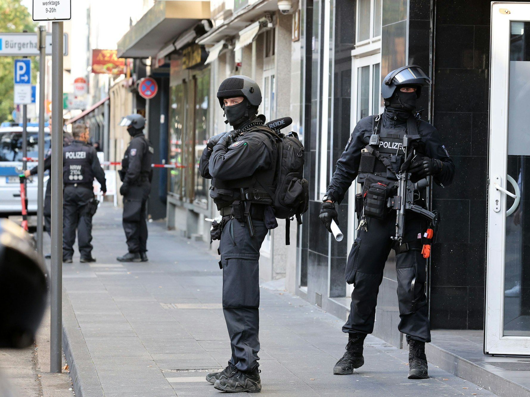 Vermummte und schwer bewaffnete Einsatzkräfte stehen auf dem Gehweg.