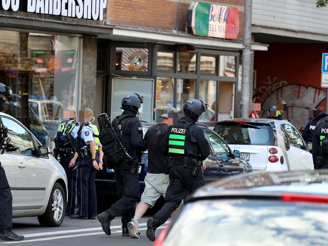 Einsatzkräfte führen einen Mann weg. Auf beiden Seiten der Fahrbahn stehen Autos sowie weitere Einsatzkräfte der Polizei.