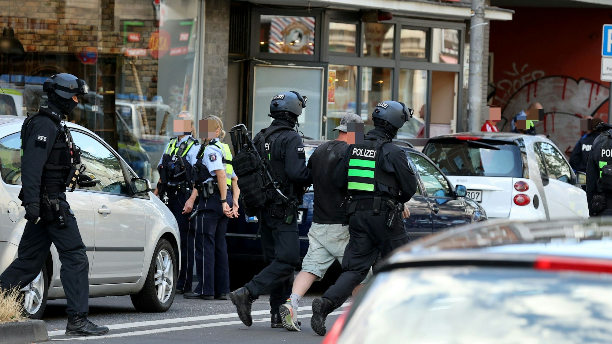 Einsatzkräfte führen einen Mann weg. Auf beiden Seiten der Fahrbahn stehen Autos sowie weitere Einsatzkräfte der Polizei.