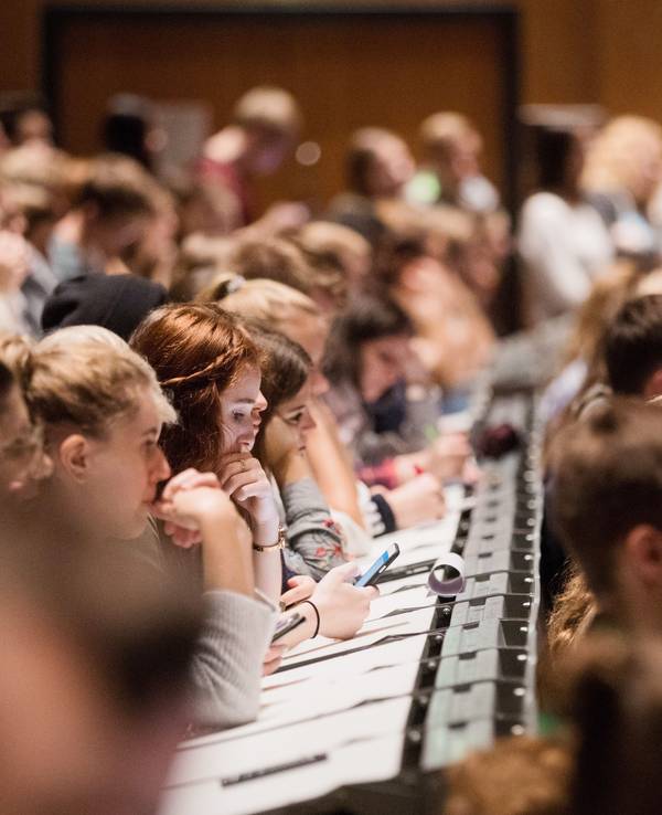 Studenten und Studentinnen verfolgen im Hörsaal im Hauptgebäude der Universität in Köln die Erstsemesterbegrüßung.