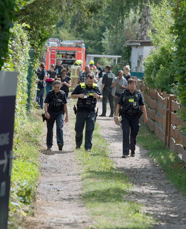 Einsatzkräfte der Polizei und Feuerwehr stehen auf einem Grundstück und untersuchen Spuren.