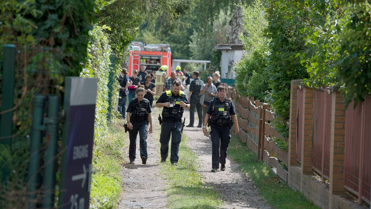 Einsatzkräfte der Polizei und Feuerwehr stehen auf einem Grundstück und untersuchen Spuren.