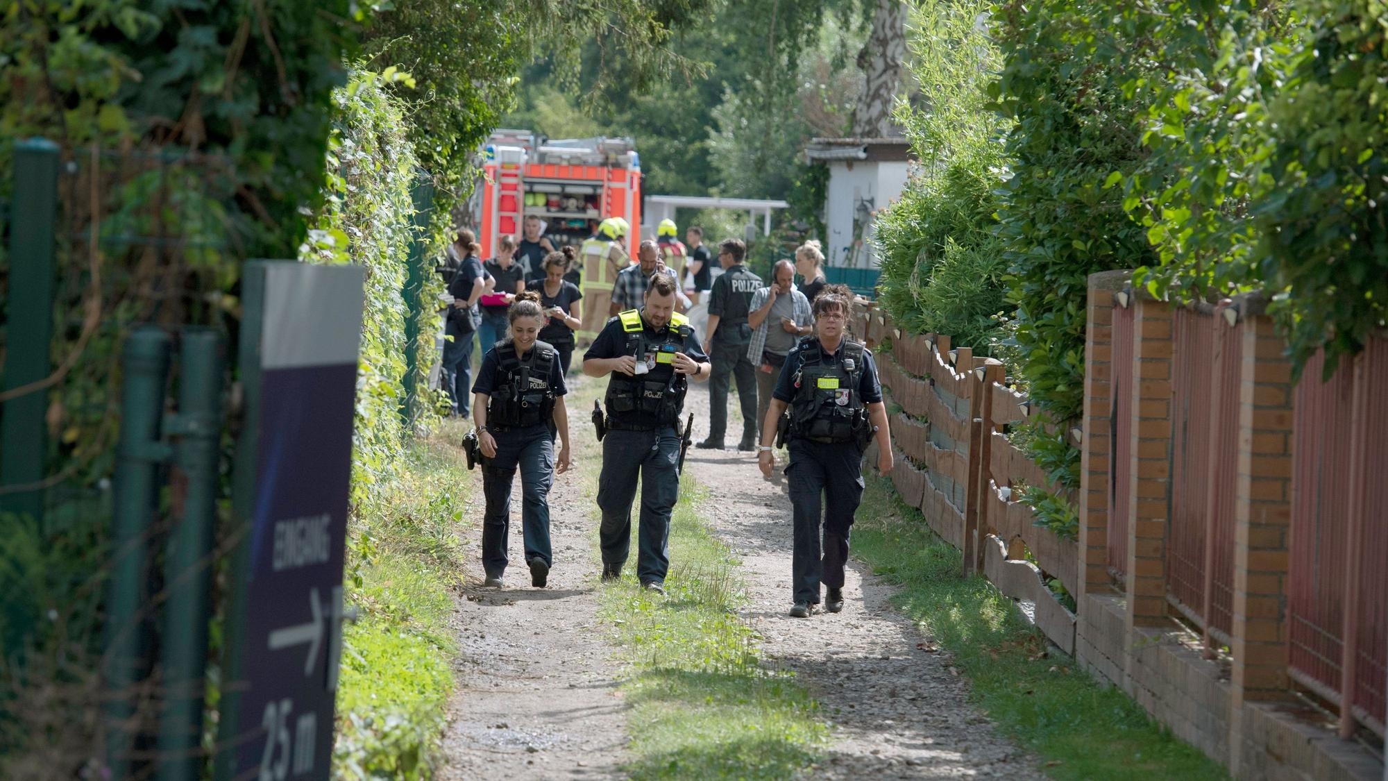 Einsatzkräfte der Polizei und Feuerwehr stehen auf einem Grundstück und untersuchen Spuren.