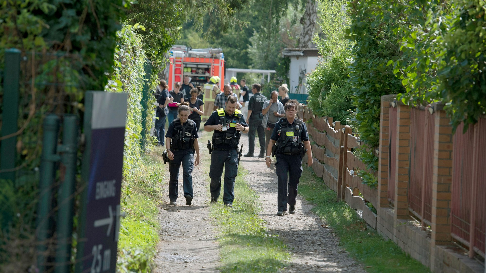Einsatzkräfte der Polizei und Feuerwehr stehen auf einem Grundstück und untersuchen Spuren.