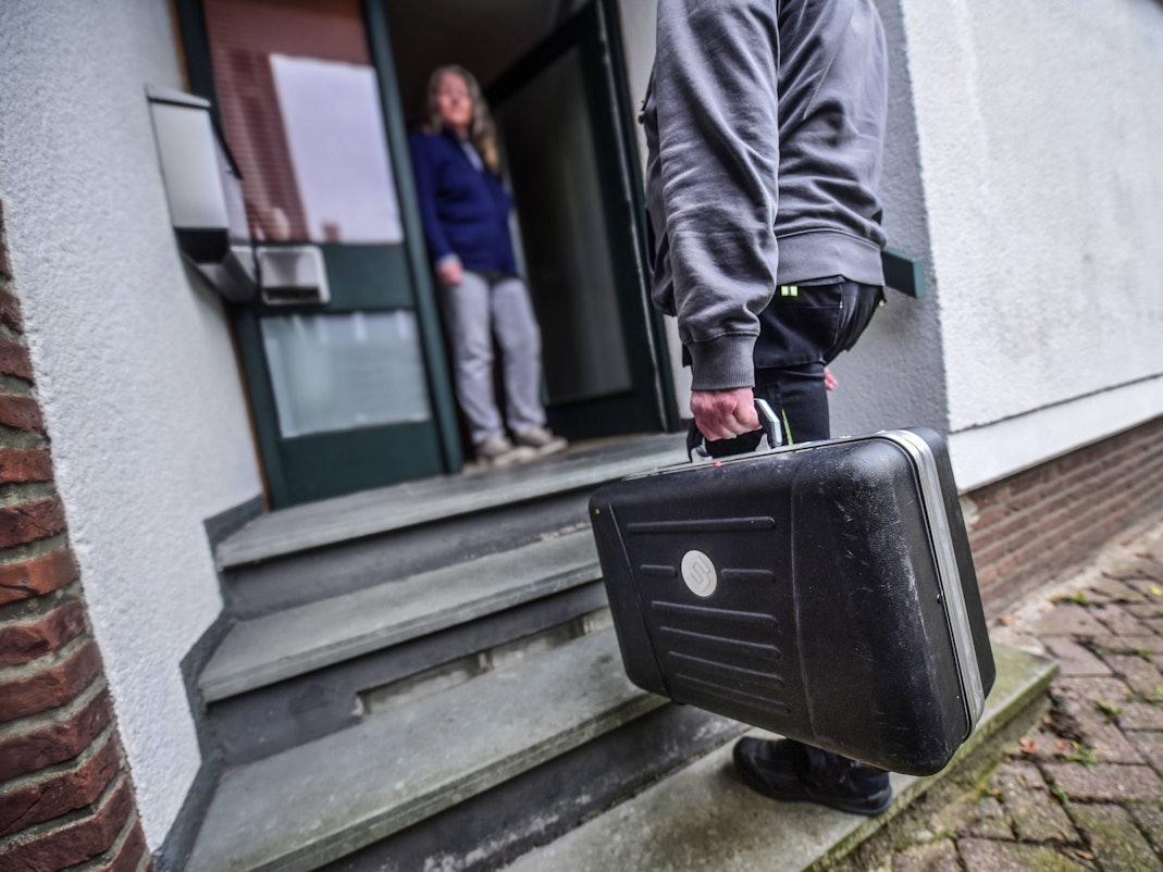 Ein Mann mit Handwerker-Koffer steht vor der geöffneten Haustür einer Frau.