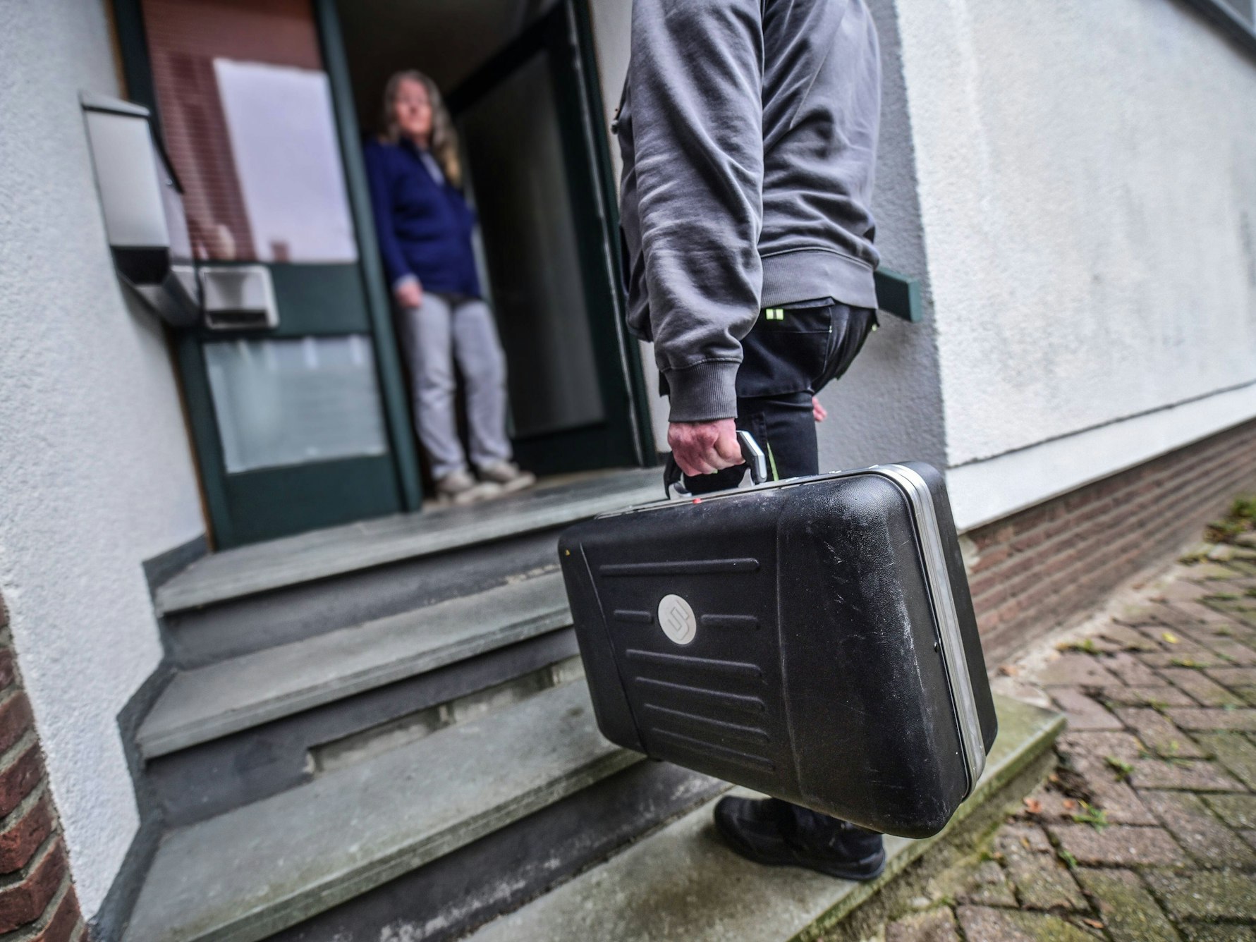 Ein Mann mit Handwerker-Koffer steht vor der geöffneten Haustür einer Frau.