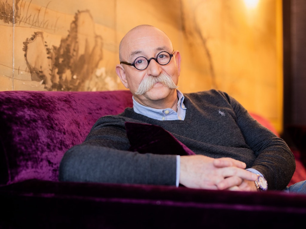 Horst Lichter sitzt gemütlich in einem roten Sessel und lächelt dabei in die Kamera.