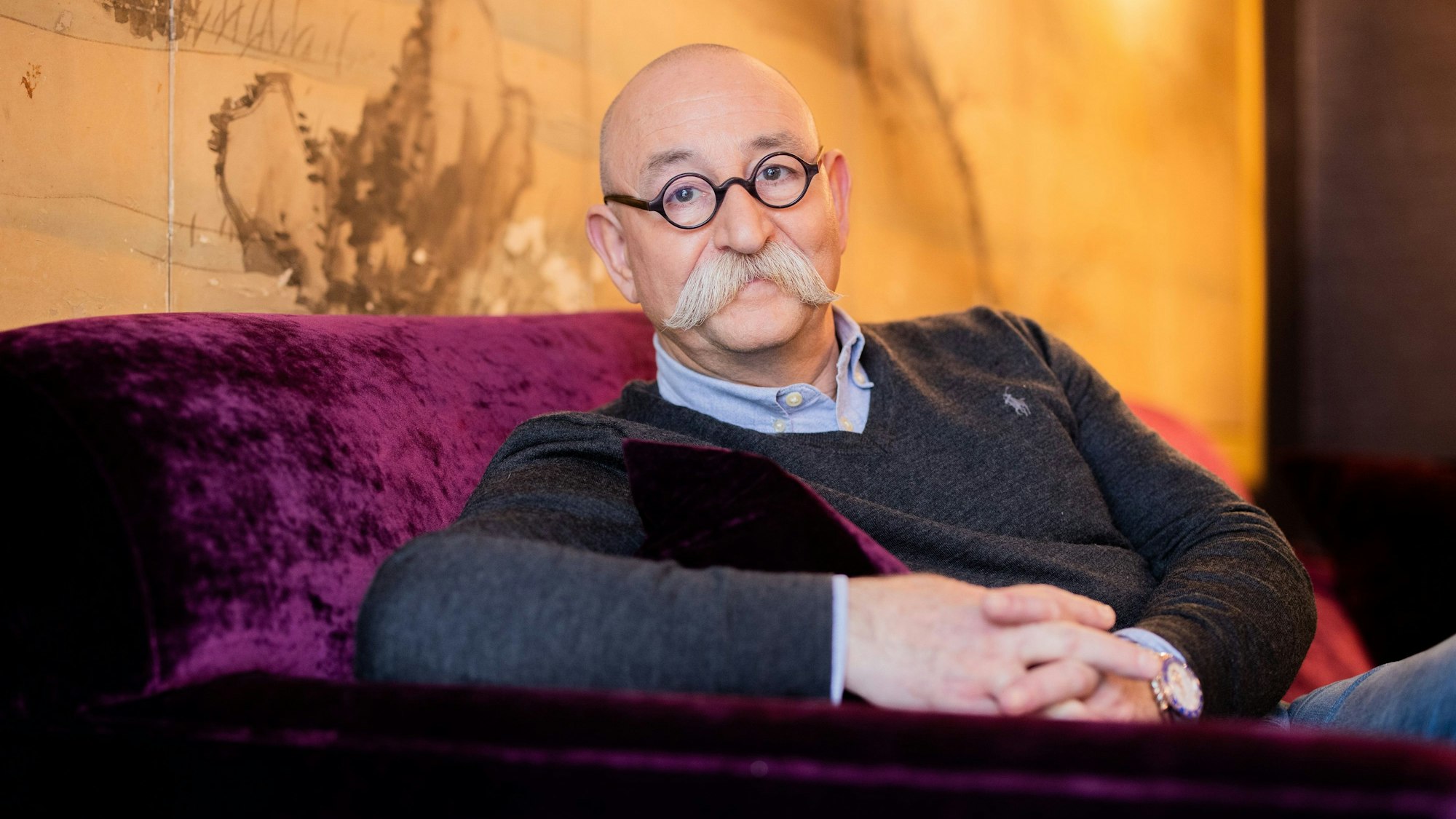 Horst Lichter sitzt gemütlich in einem roten Sessel und lächelt dabei in die Kamera.