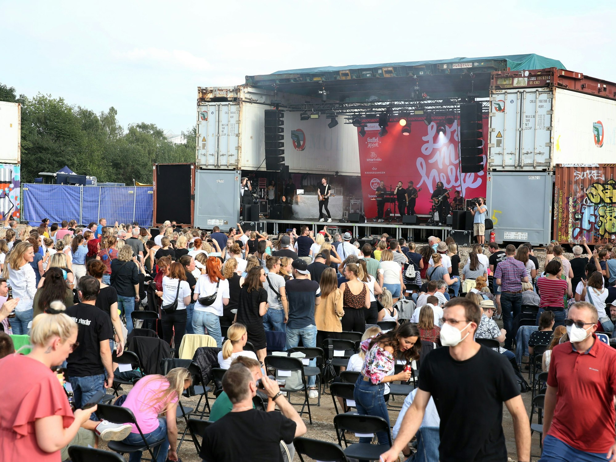 Publikum sitzt zu einer Open-Air-Bühne gewandt, auf der eine Band spielt.