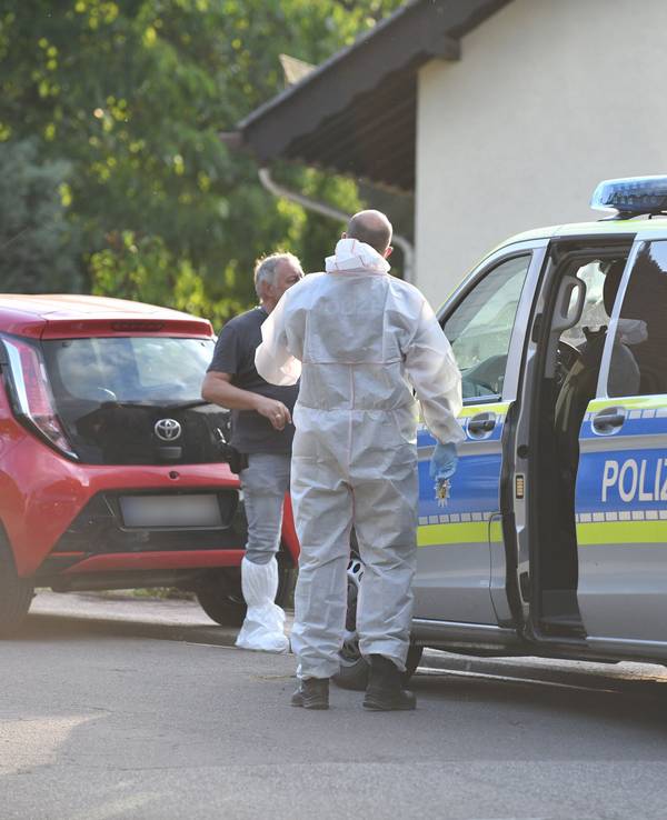 Einsatzkräfte der Polizei und Spurensicherung stehen vor einem Haus.