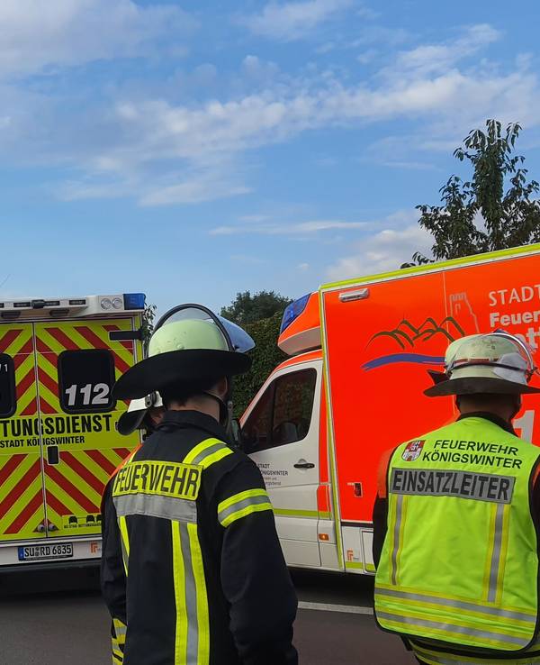 Zwei Feuerwehrmänner stehen mit dem Rücken zur Kamera vor ihren Einsatzwagen auf der Autobahn.
