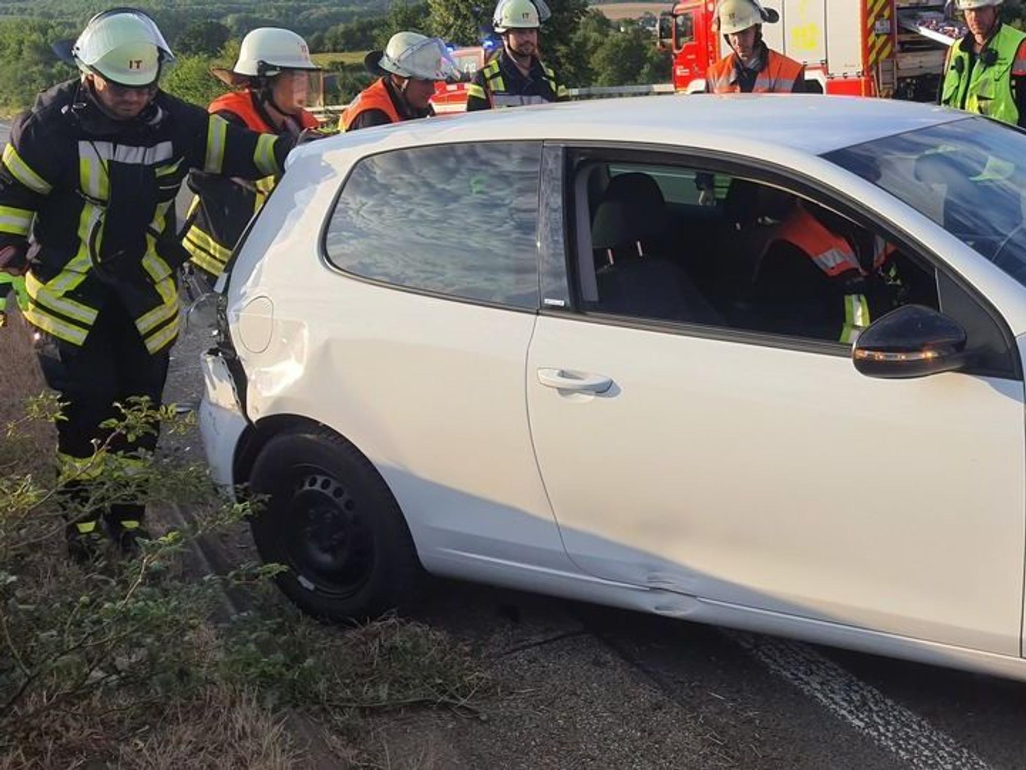 Einsatzkräfte der Feuerwehr stehen um ein demoliertes Unfallauto auf der Autobahn.