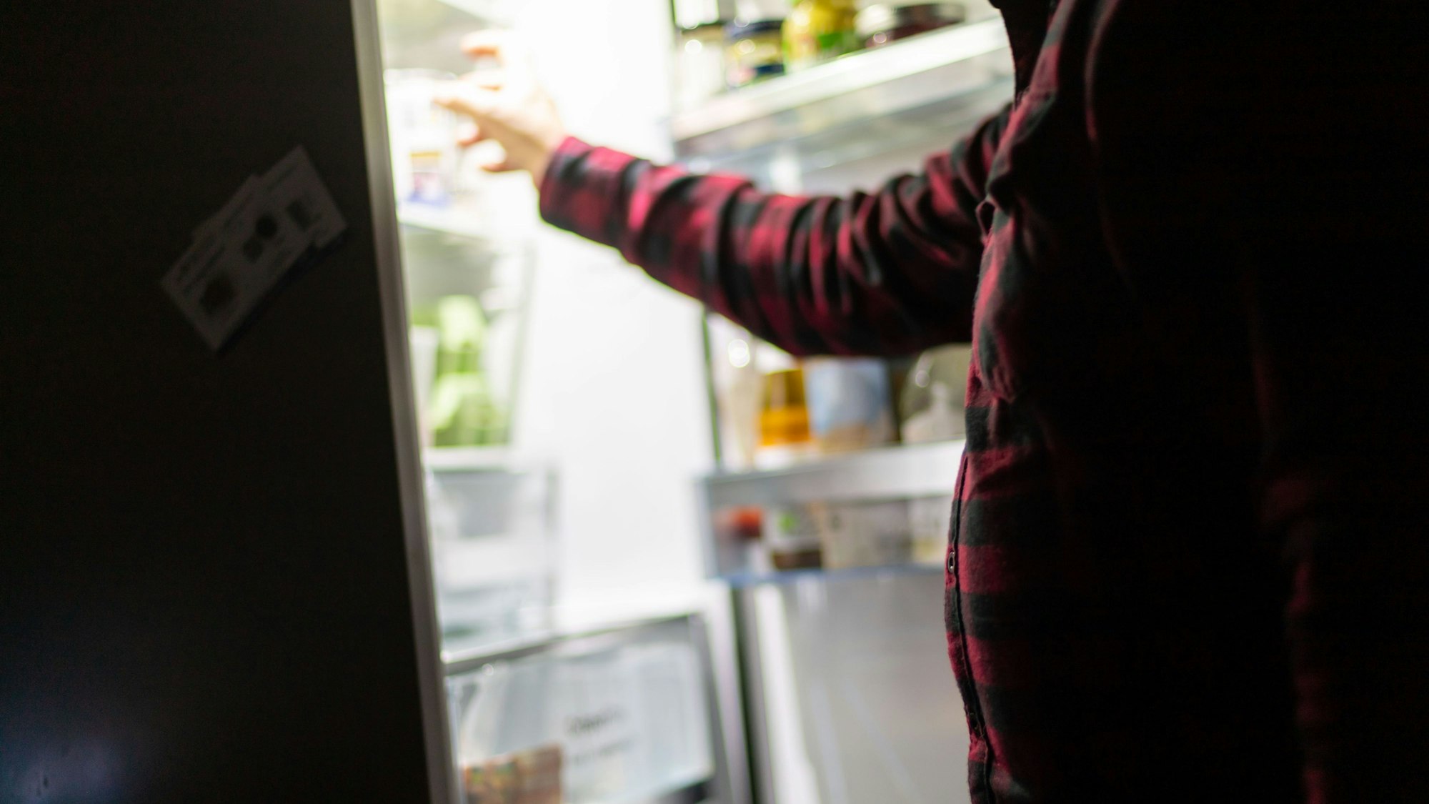 Ein Mann nimmt etwas aus dem Kühlschrank.+