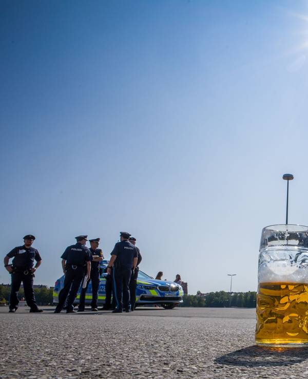 Ein verlassener, halb gefüllter Bierkrug auf dem Asphalt. Im Hintergrund stehen Polizisten neben Polizeifahrzeugen.