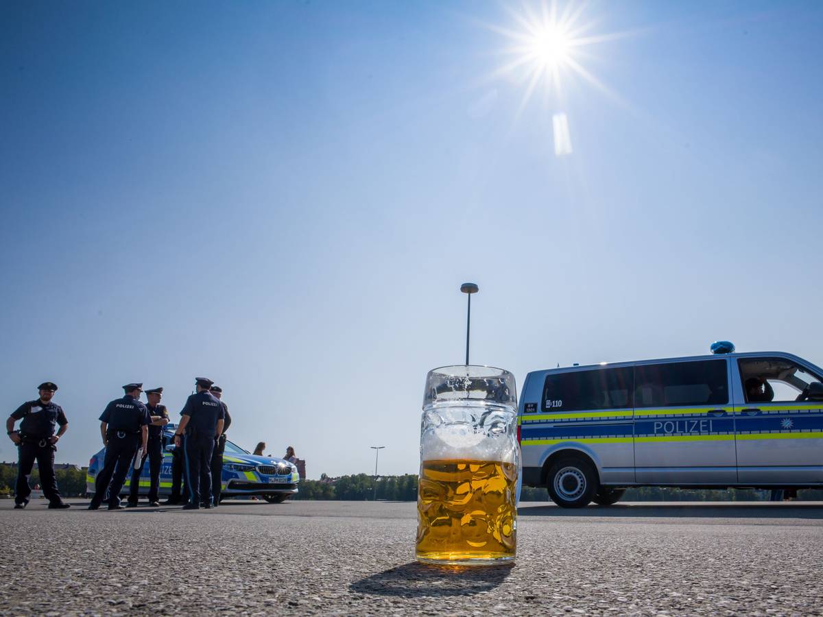 Ein verlassener, halb gefüllter Bierkrug auf dem Asphalt. Im Hintergrund stehen Polizisten neben Polizeifahrzeugen.