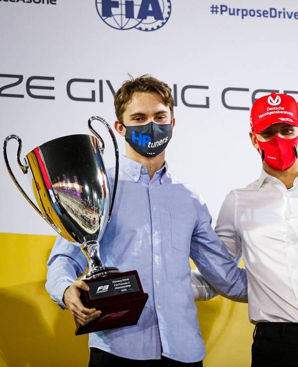 Oscar Piastri und Mick Schumacher tragen beide jeweils einen Pokal und blicken in die Kamera.