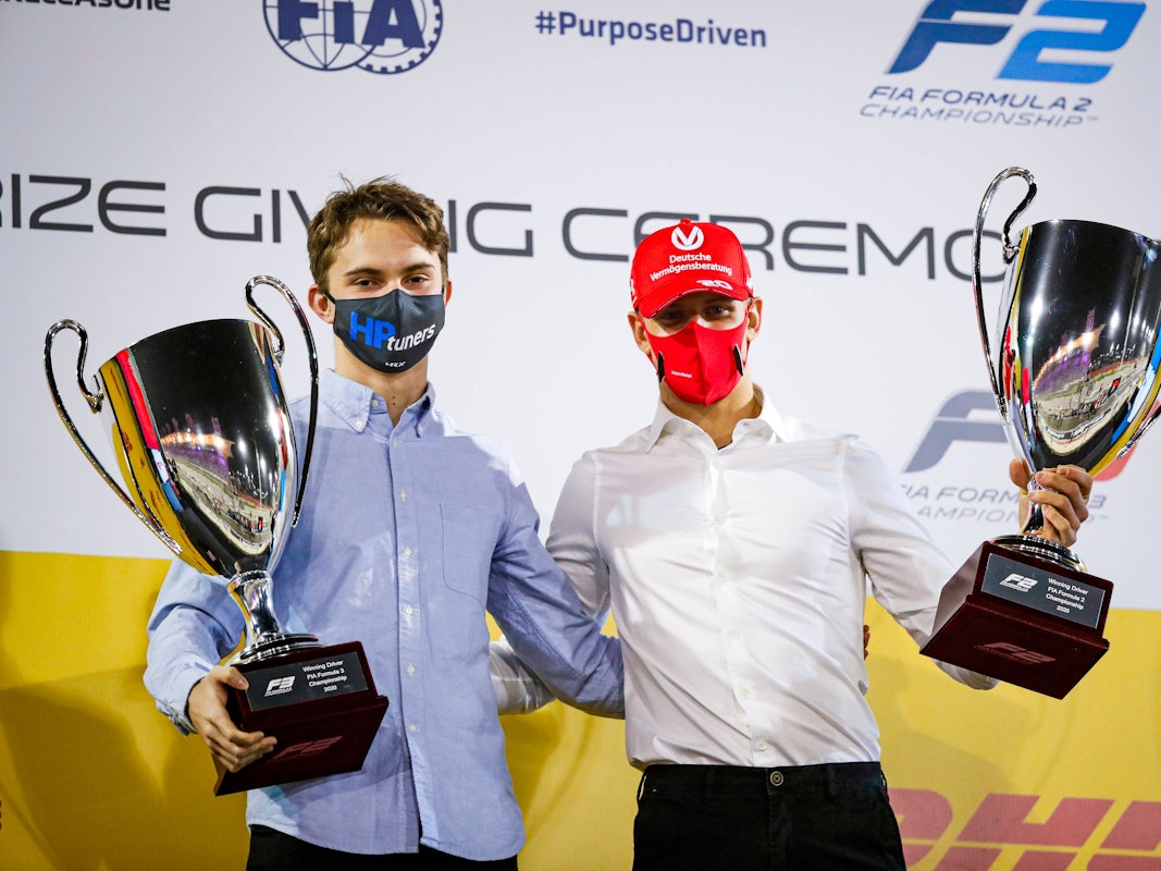Oscar Piastri und Mick Schumacher tragen beide jeweils einen Pokal und blicken in die Kamera.