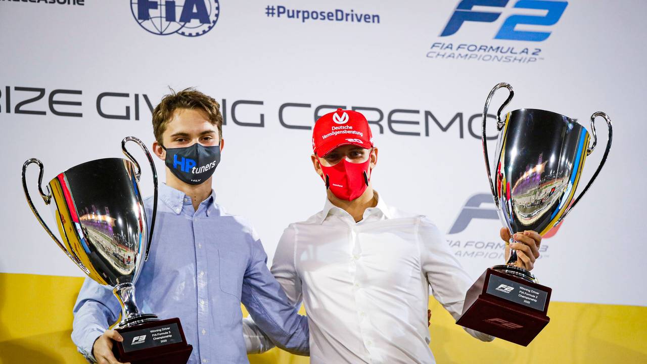 Oscar Piastri und Mick Schumacher tragen beide jeweils einen Pokal und blicken in die Kamera.