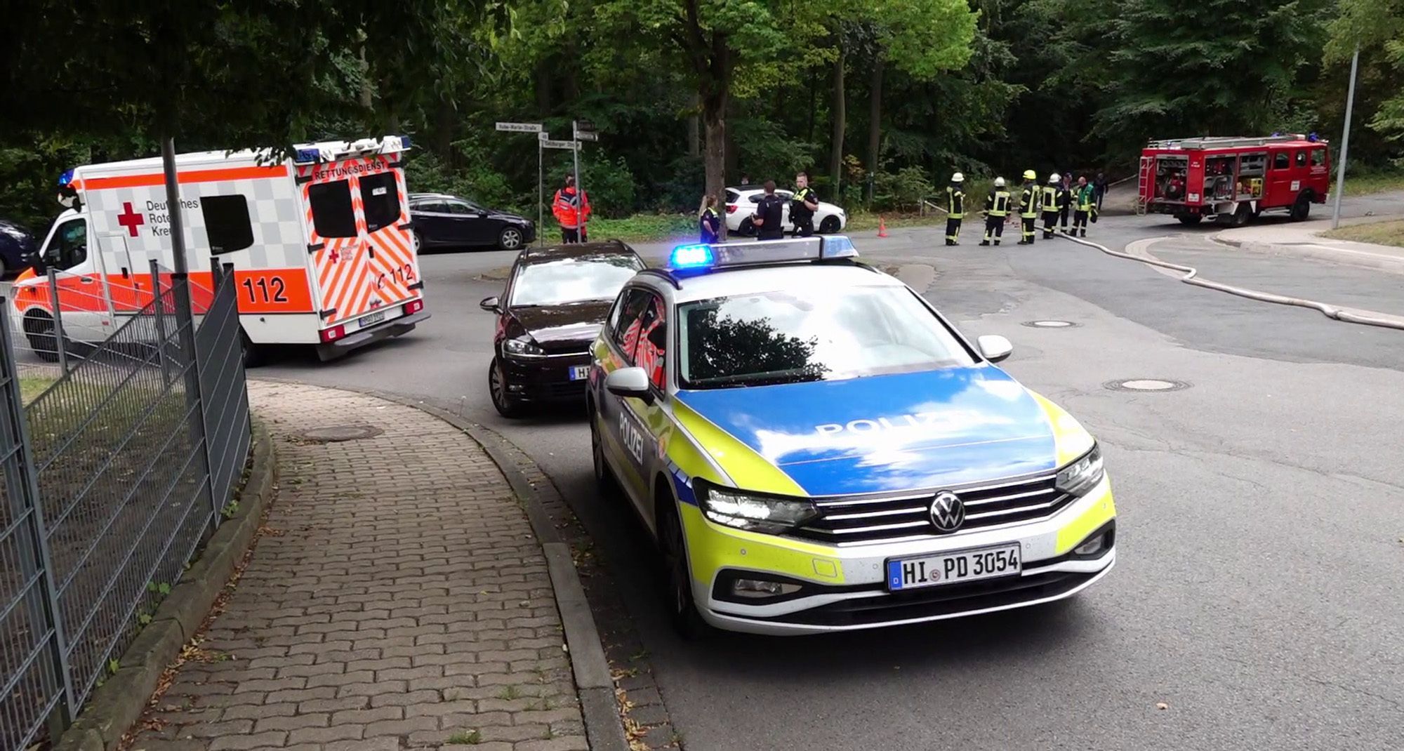 Ein Polizeifahrzeug und ein Krankenwagen stehen an einer Unfallstelle. In Köln-Müngersdorf kam es zu einer Kollision zwischen einem Roller und einem Kleinwagen, der Rollerfahrer wurde schwer verletzt.