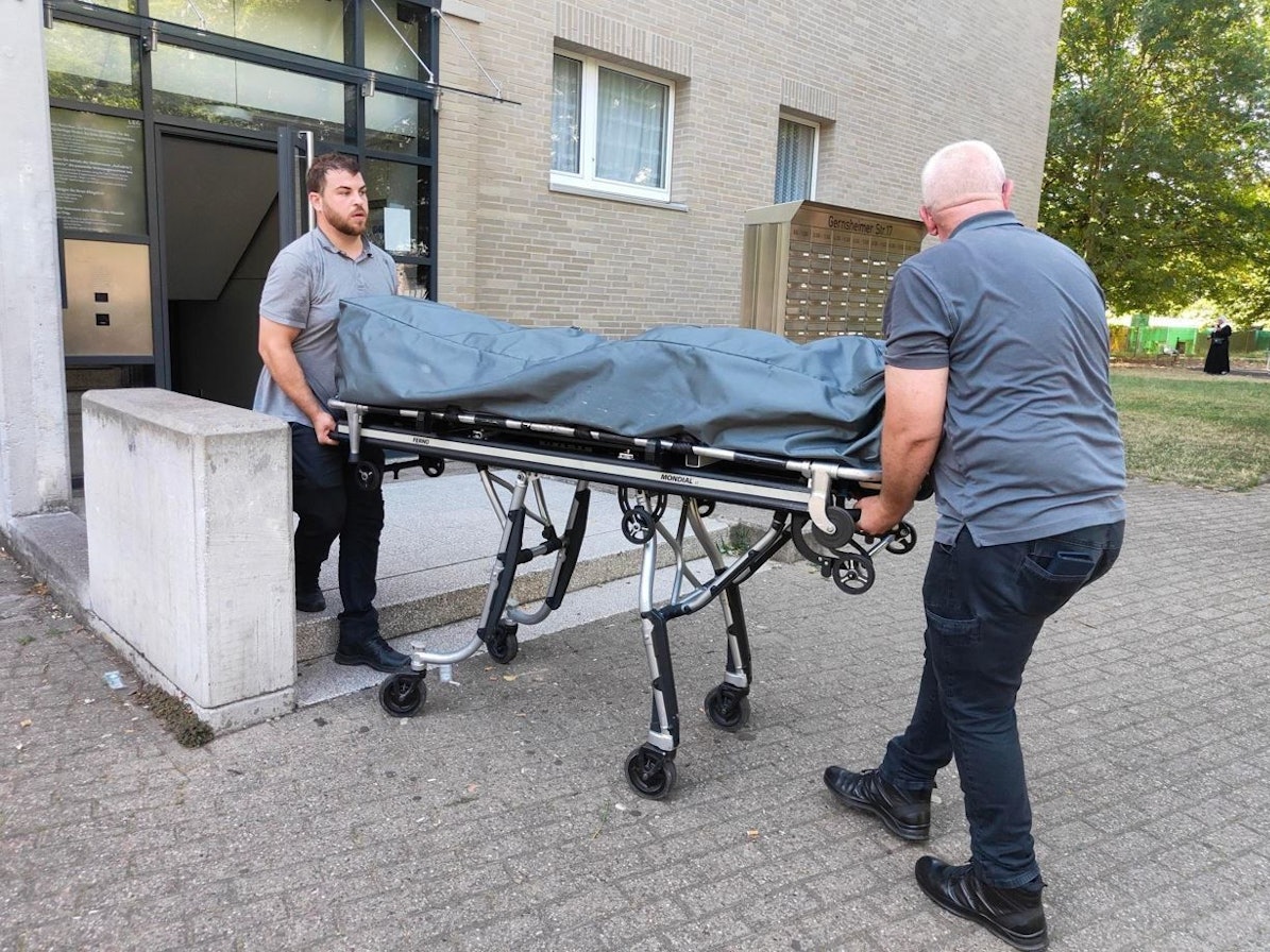 Zwei Bestatter bringen die Leiche auf einer Bahre aus dem Mehrfamilienhaus.