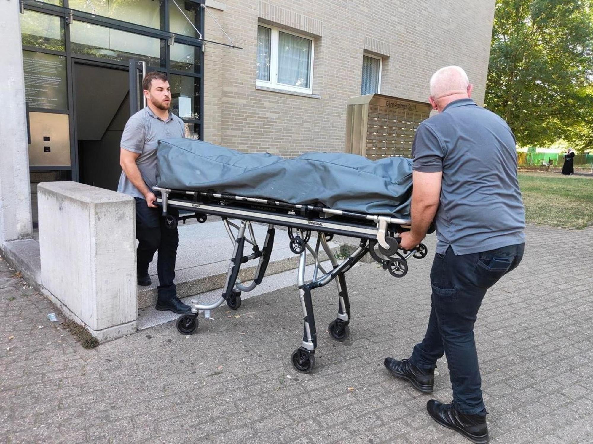 Zwei Bestatter bringen die Leiche auf einer Bahre aus dem Mehrfamilienhaus.