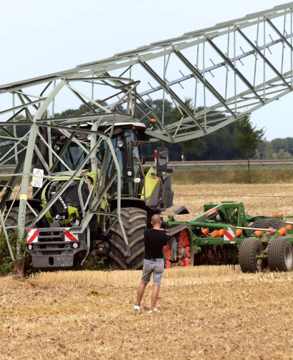 Ein Traktor steht auf einem Feld unter einem umgeknickten Strommast.
