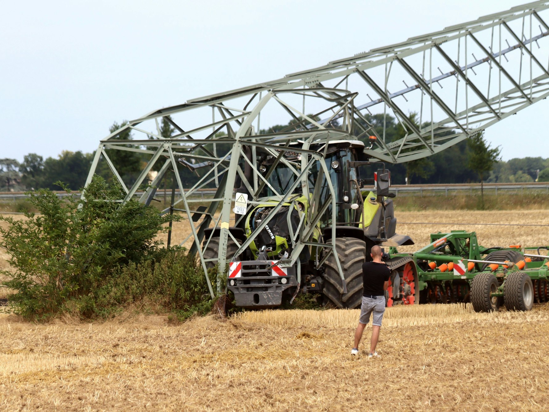 Ein Traktor steht auf einem Feld unter einem umgeknickten Strommast.