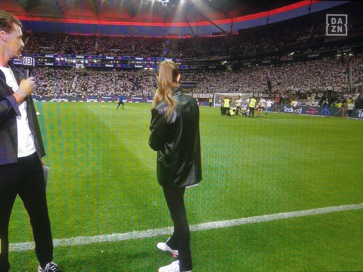 Laura Wontorra und Sandro Wagner blicken während der Halbzeit-Analyse bei DAZN auf den Rasen in Frankfurt, wo sich Fan-Chaoten einen Streit mit Ordnern liefern.