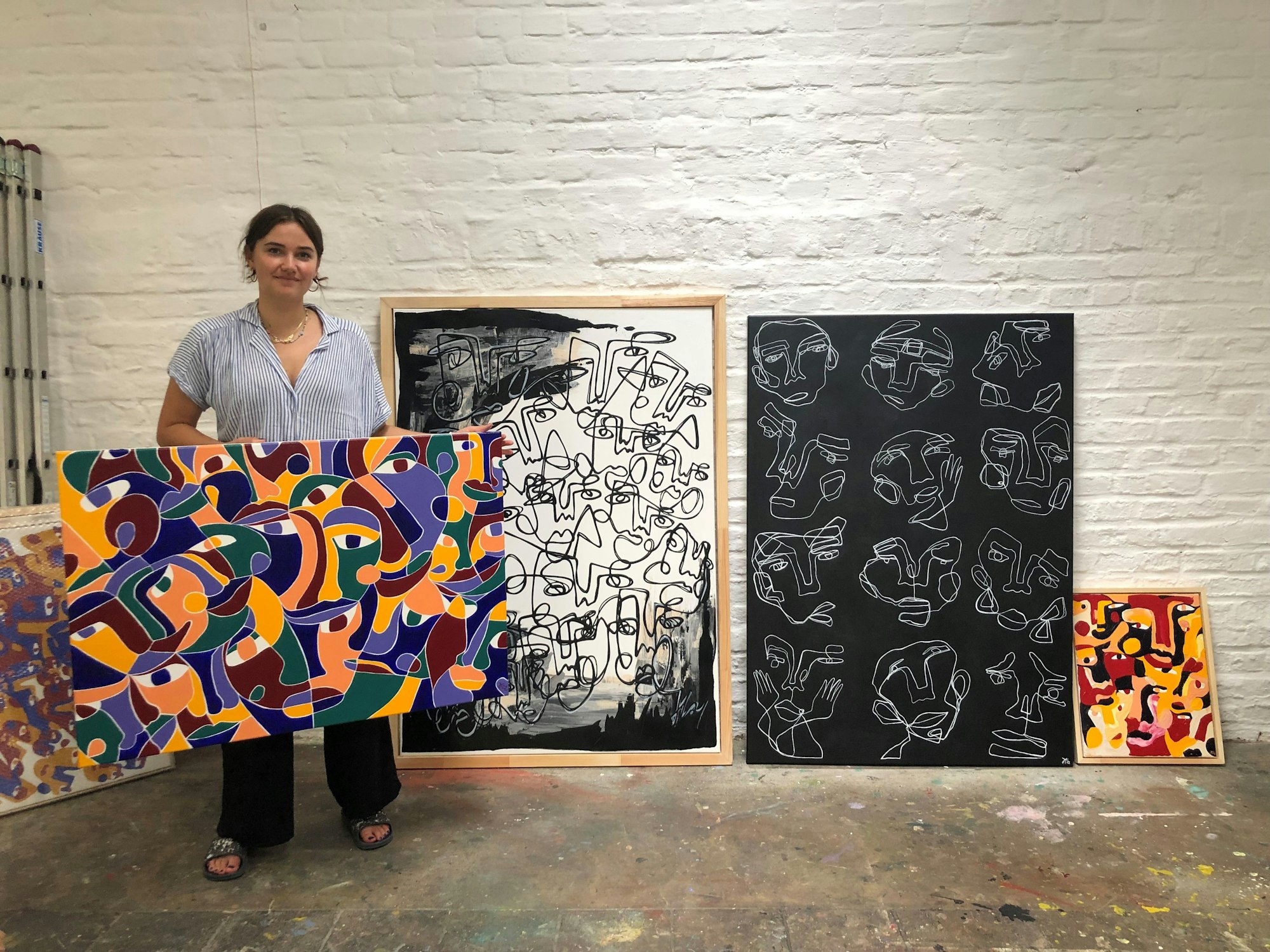 Hanna Hodler steht in ihrem Atelier vor ihren Bilder und hält eins in der Hand.