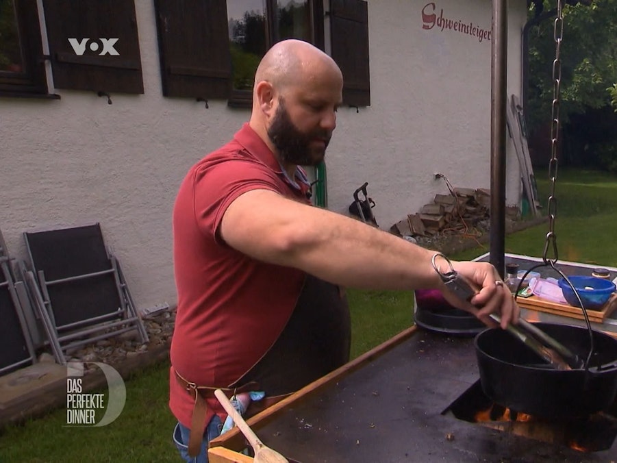 Robert fuchtelt mit einer Grillzange über dem offenen Feuer herum.