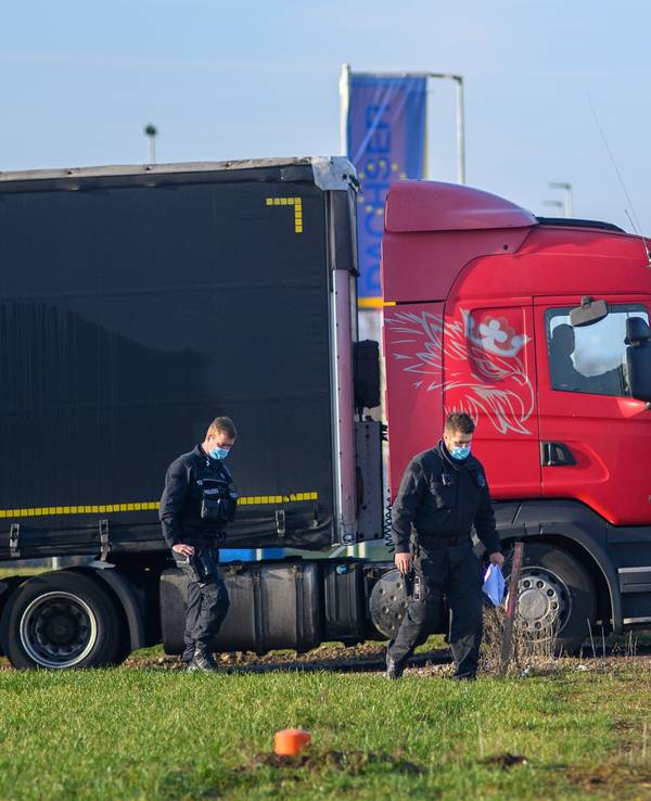 Polizisten gehen zu ihrem Fahrzeug während dahinter ein Lastwagen seinen Stellplatz verlässt.