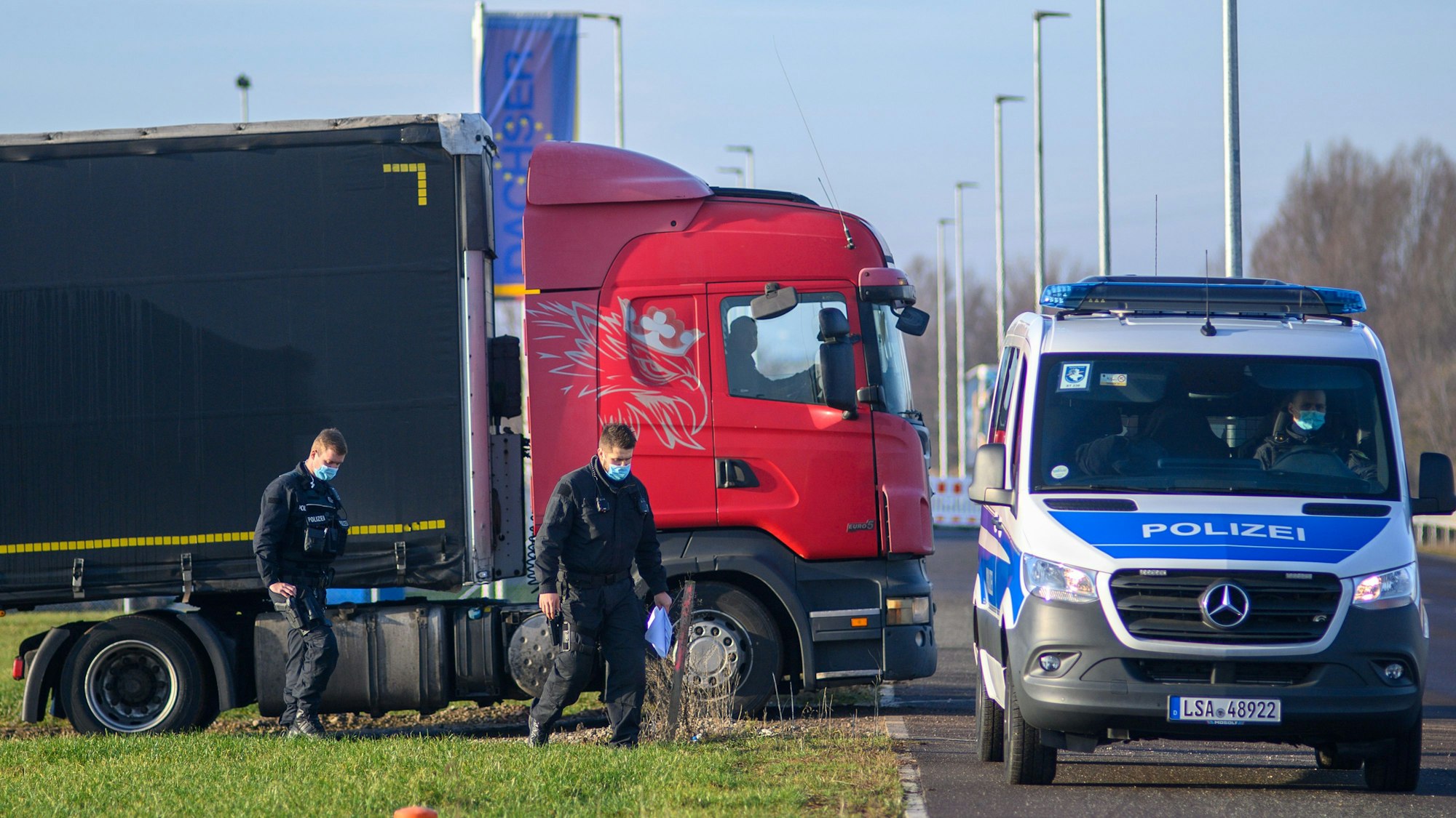 Polizisten gehen zu ihrem Fahrzeug während dahinter ein Lastwagen seinen Stellplatz verlässt.