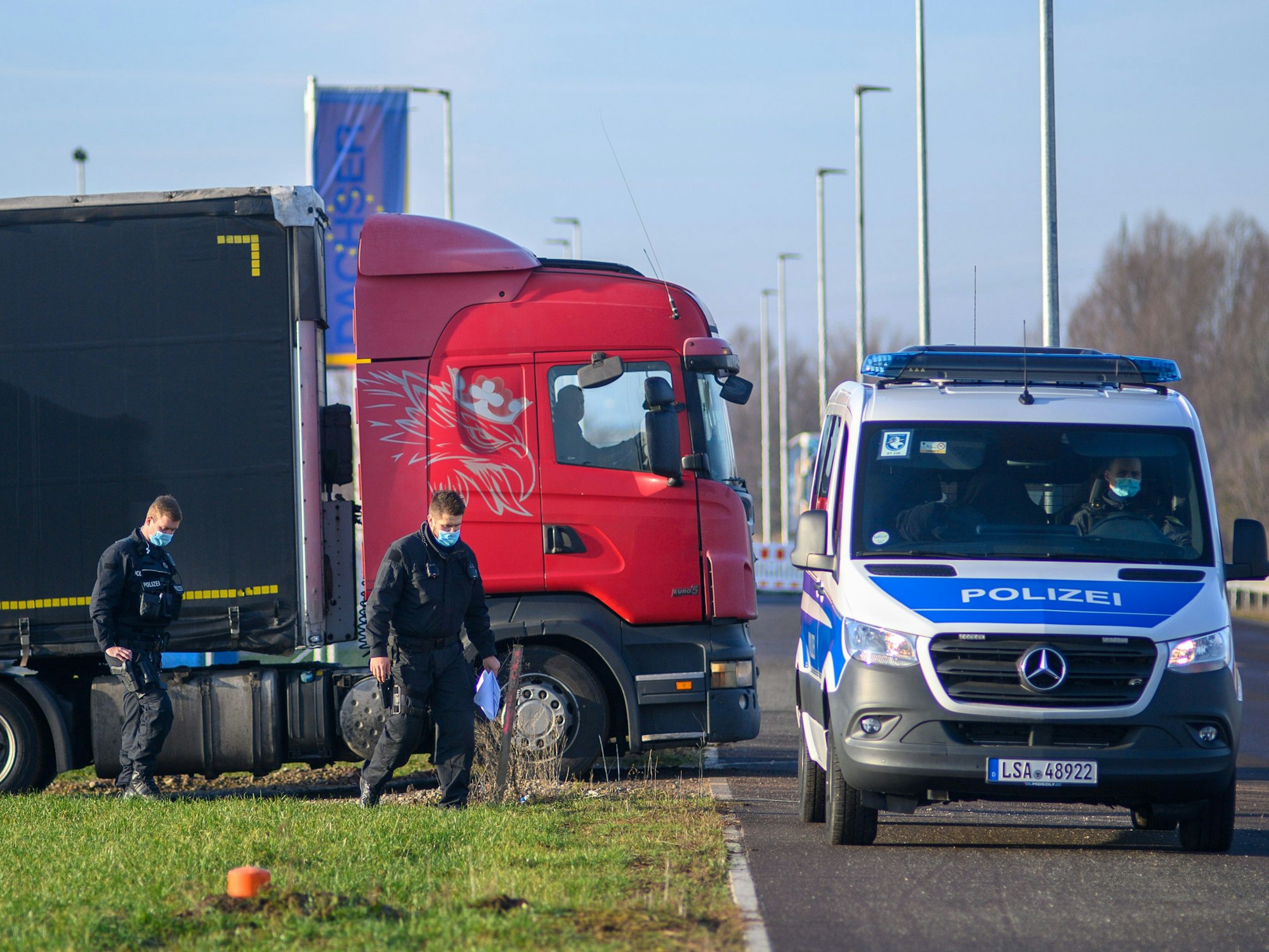 Polizisten gehen zu ihrem Fahrzeug während dahinter ein Lastwagen seinen Stellplatz verlässt.