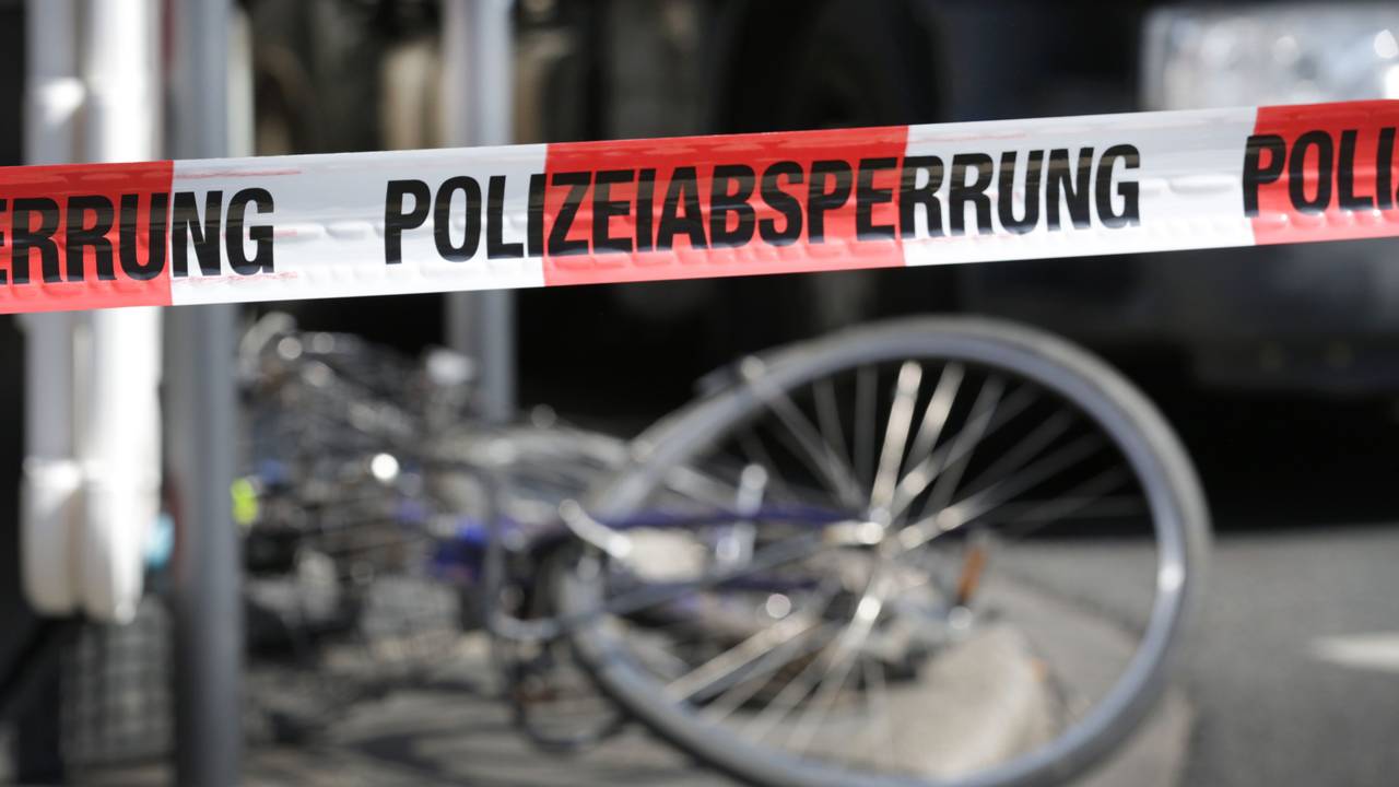 Demoliertes Fahrrad liegt auf einer Straße, davor ein Absperrband der Polizei.