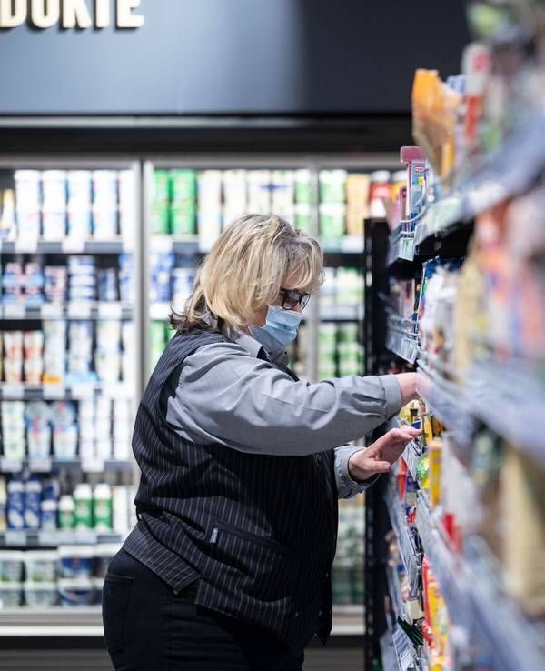 Eine Angestellte sortiert im Einzelhandelsgeschäft „Staufers Markthalle“ Regale ein und trägt einen Mundschutz. Nach knapp zwei Jahren ist in großen Teilen Deutschlands die Maskenpflicht im Einzelhandel entfallen. Beschäftigte und Kunden entscheiden selbst, ob sie weiterhin eine Maske tragen. +++ dpa-Bildfunk +++
