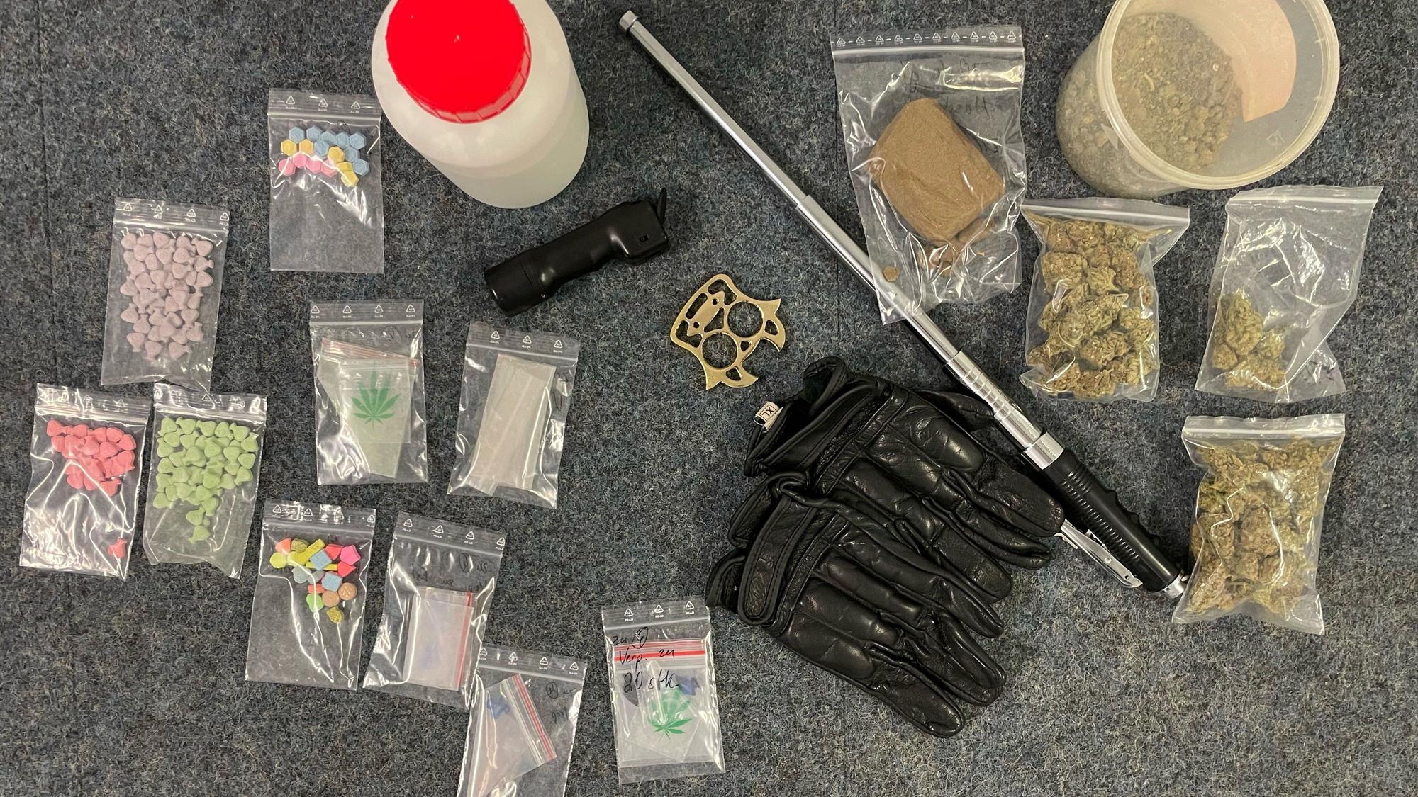 In kleinen Tütchen befinden sich diverse Drogen, dazwischen liegen Waffen wie ein Teleskopschlagstock.