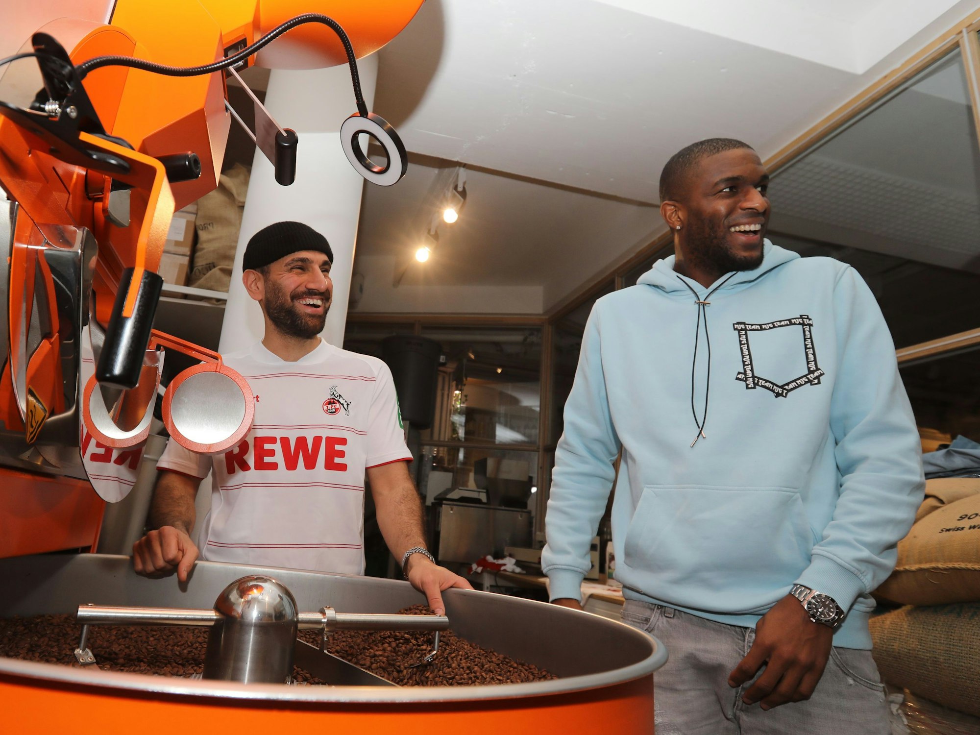 Anthony Modeste und Rafet Aydogdu stehen zusammen an einer Kaffee-Röstmaschine.
