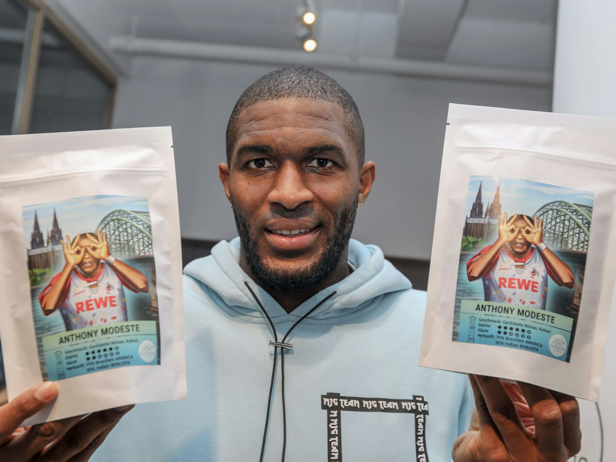 Anthony Modeste zeigt eine Kaffee-Packung mit seinem Bild in die Kamera.