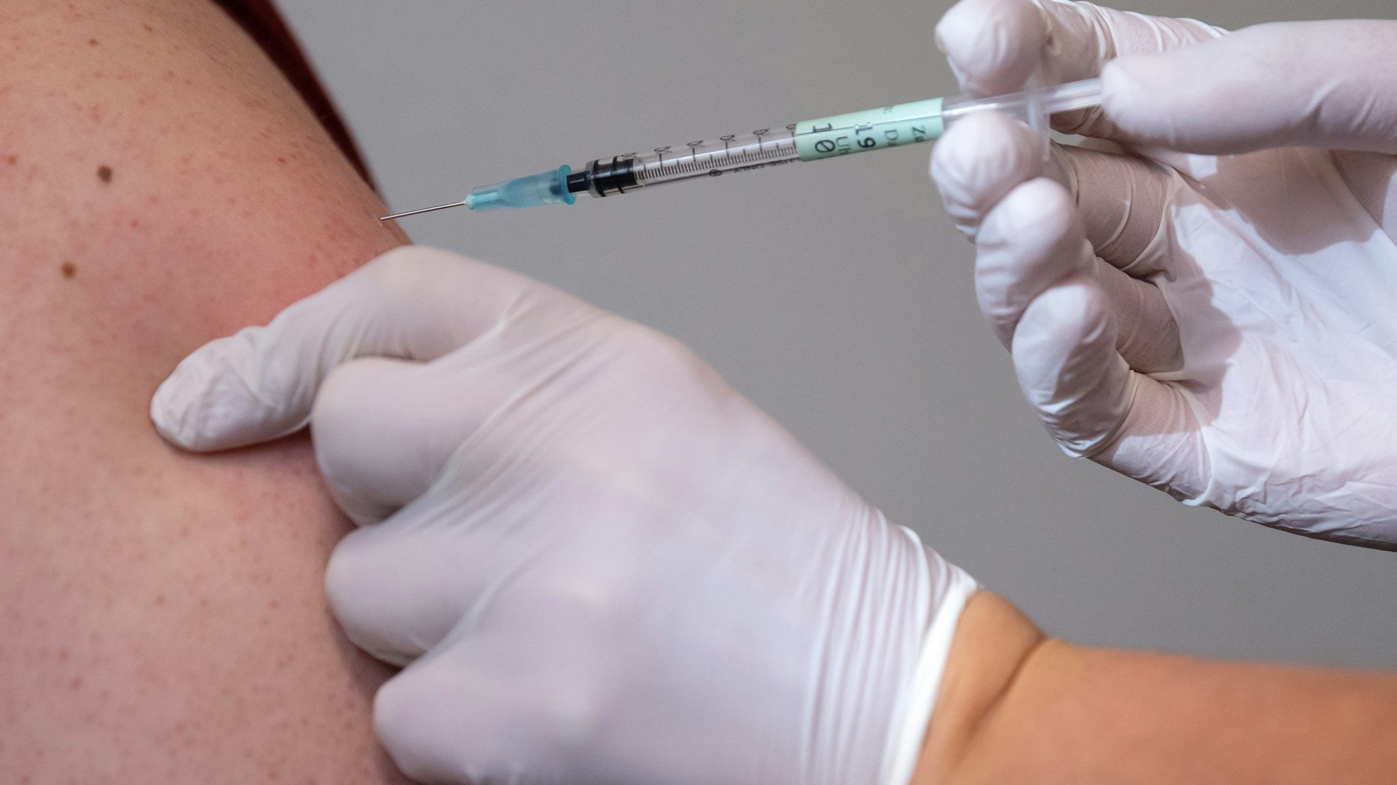 Eine Person sticht einer anderen Person eine Spritze in den Oberarm.