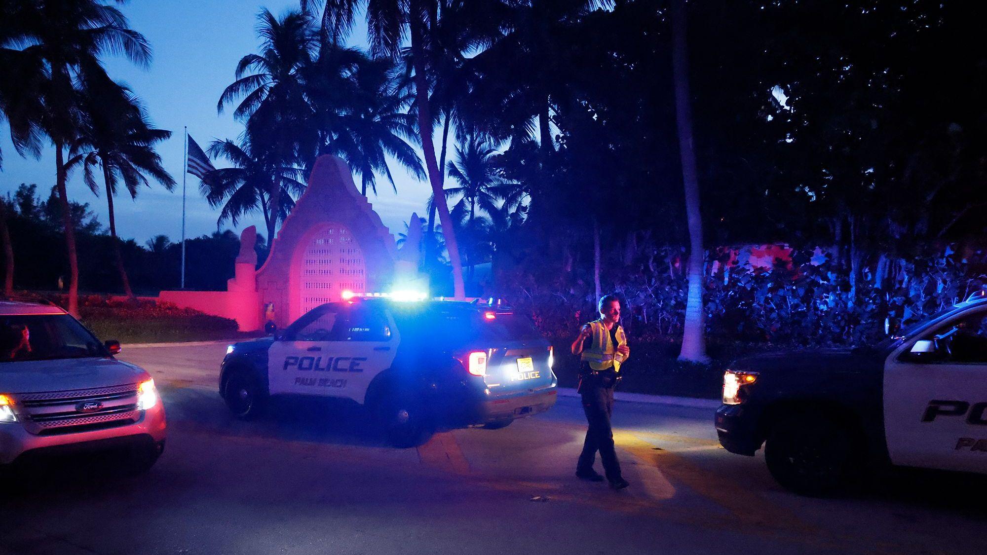 Das undatierte Symbolfoto zeigt drei US-amerikanische Polizeiwagen mit Blaulicht und einen uniformierten Polizisten vor einem Tor. Überall stehen Palmen.