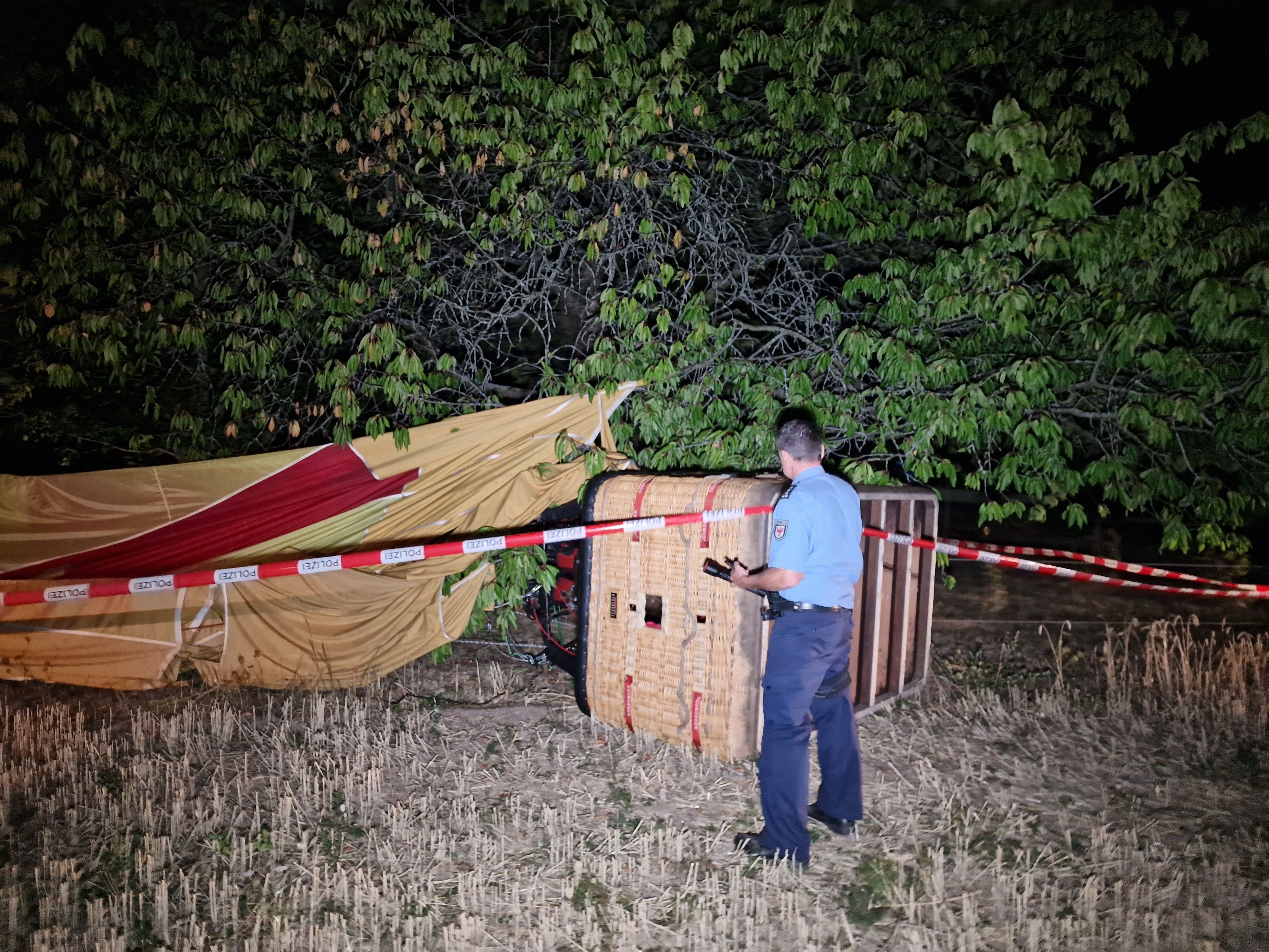 Ein Polizist inspiziert einen verunfallten Heißluftballon. Bei einem Unfall mit einem Heißluftballon ist am Montagabend ein Mann in Beelitz (Landkreis Potsdam-Mittelmark) ums Leben gekommen.