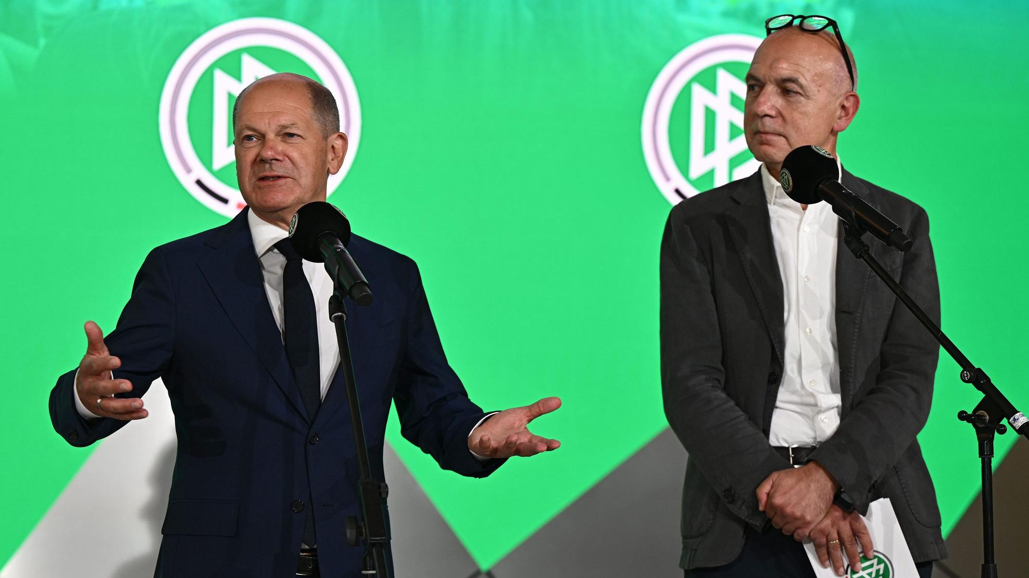 Olaf Scholz spricht neben Bernd Neuendorf.