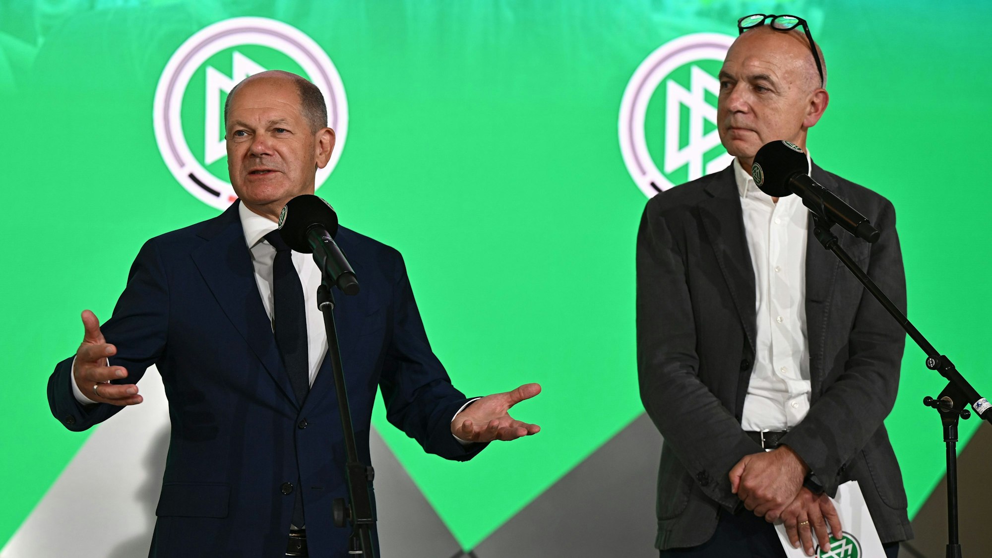 Olaf Scholz spricht neben Bernd Neuendorf.