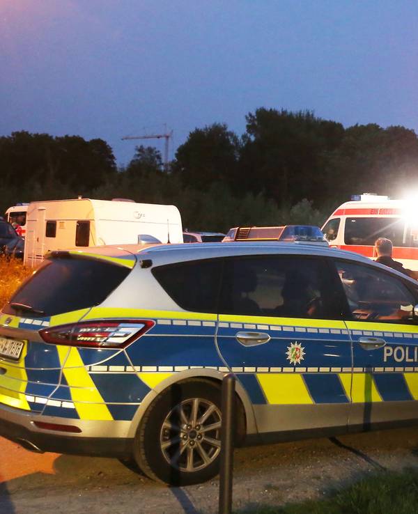 Einsatzkräfte der Polizei stehen hinter einem Rettungswagen am Einsatzort.