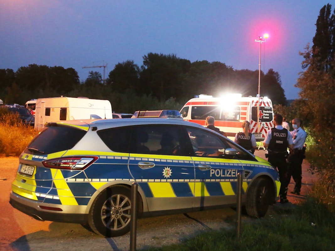 Einsatzkräfte der Polizei stehen hinter einem Rettungswagen am Einsatzort.