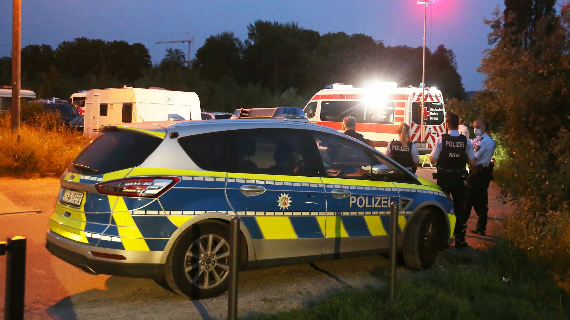 Einsatzkräfte der Polizei stehen hinter einem Rettungswagen am Einsatzort.