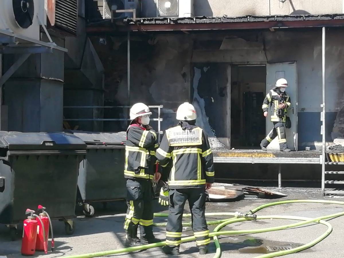 Ein Feuerwehrmann kommt aus einem Gebäude, in dem es gebrannt hat, zwei Kollegen stehen davor, zu ihren Füßen Löschschläuche.